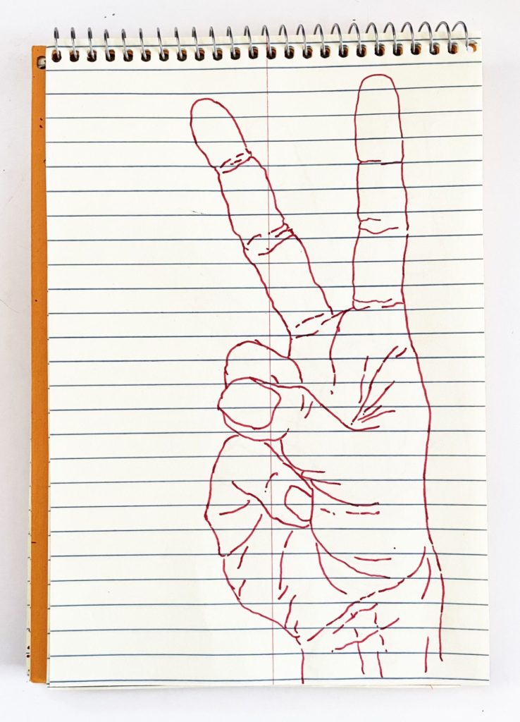 An outline handsketch of a hand shaping the ASL American manual letter “V”, in red ink on a yellow spiral bound steno notebook. 