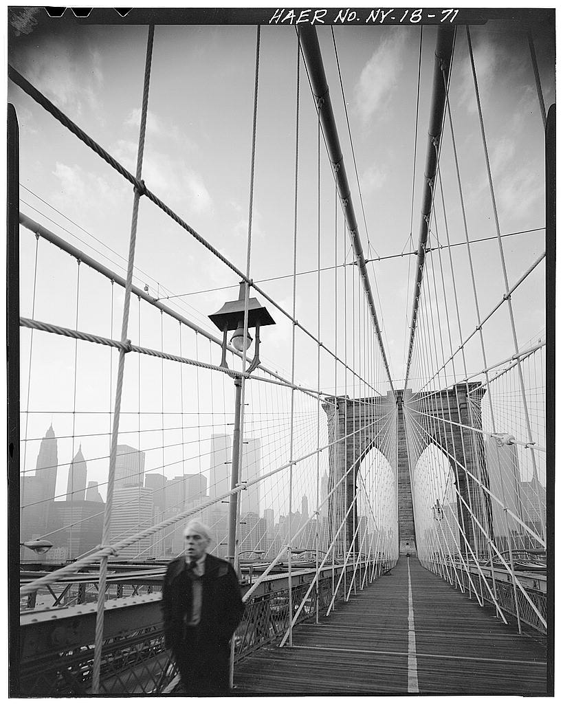 black and white photograph of the Brooklyn Bridge focused on the suspension wires with a figure breaking the bottom frame in the foreground.