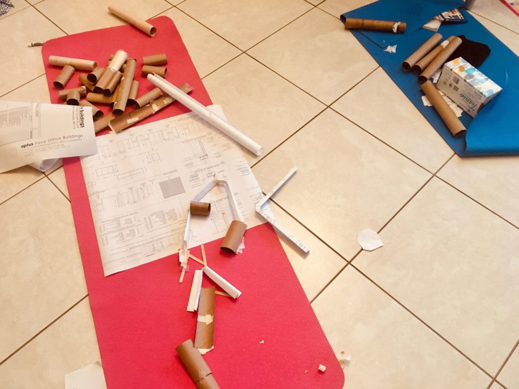 Pink and blue yoga mats on beige tile, strewn with scrap paper and toilet paper tubes.